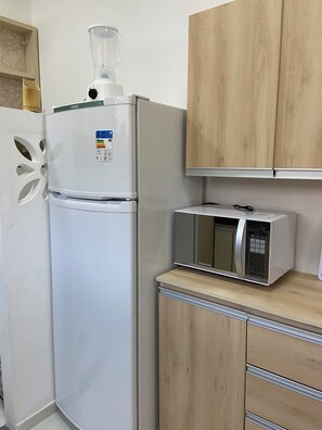 A kitchen with a white refrigerator, a blender, a microwave, and wooden cabinets. - 207 Apto 2 Qtos Lindo (Belém)