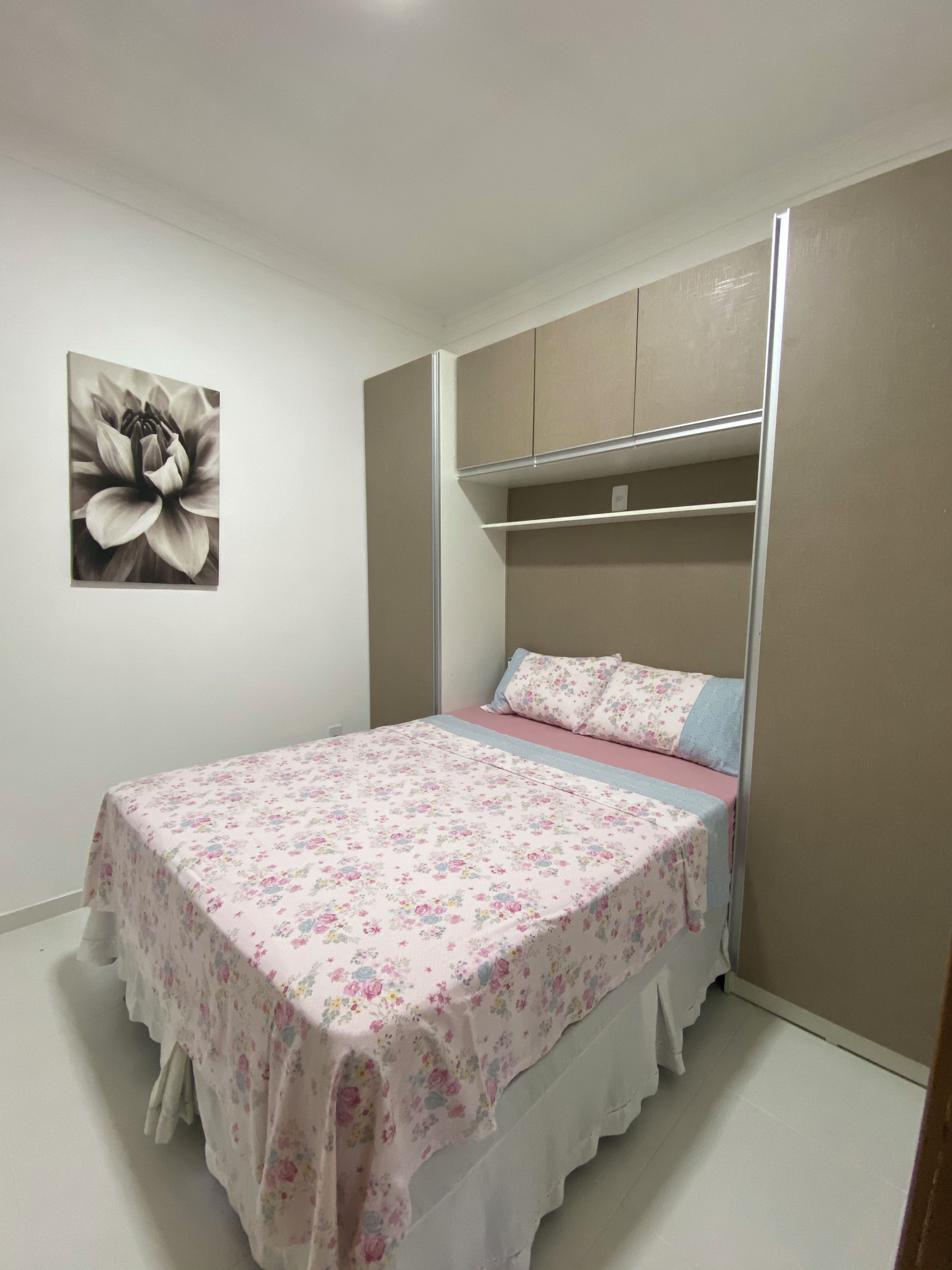Ein Schlafzimmer mit einem Bett, einem Wandregal und einer blumigen Tagesdecke.