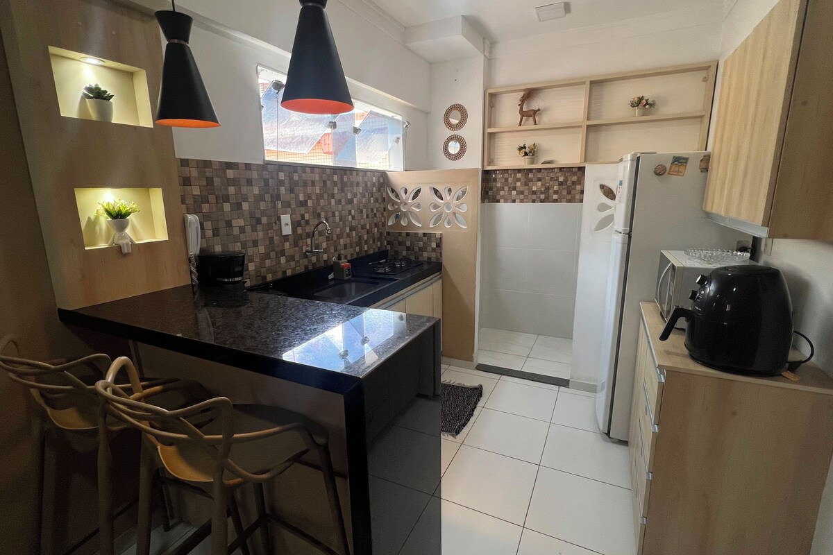 A compact kitchen with a central island, bar stools, a refrigerator, and a microwave.