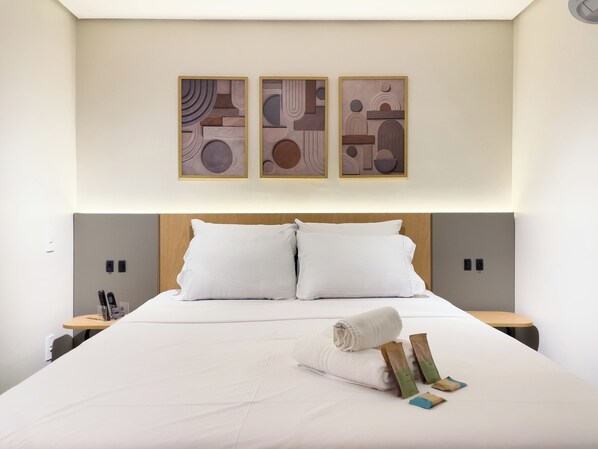 A hotel room with a large bed, two bedside tables, and three abstract wall art pieces.