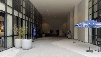 A modern building with large windows, a reception desk, and a blue umbrella with a phone number.