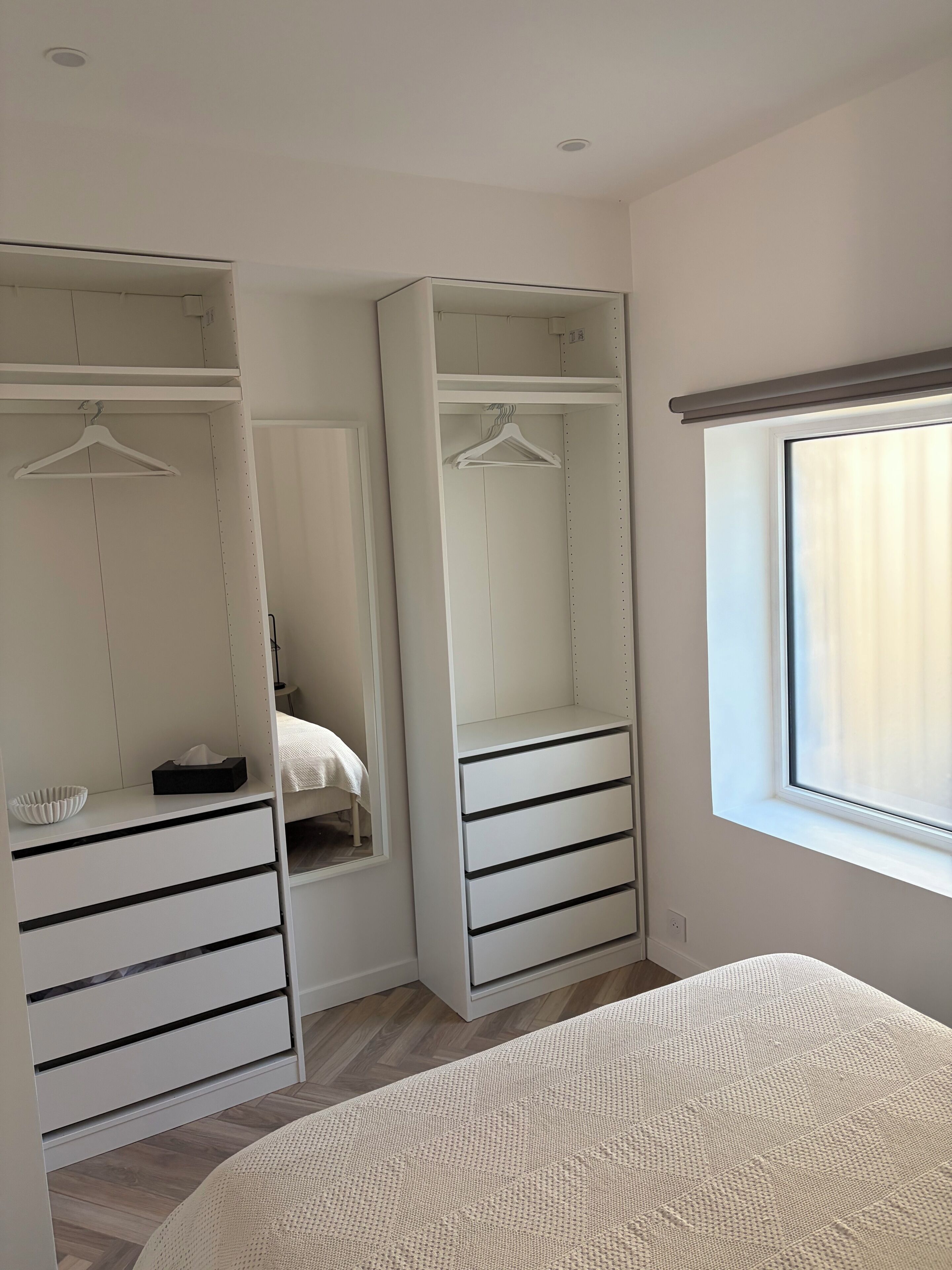 A bedroom with a large bed, a wardrobe with multiple drawers, a bedside table, and a window with curtains.