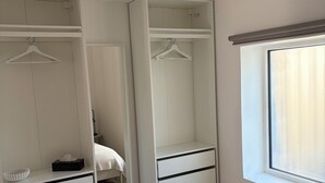 Un dormitorio con una cama grande, un armario con varios cajones, una mesita de noche y una ventana con cortinas.