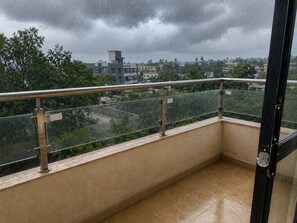 A balcony with a metal railing, a tiled floor, and a view of a residential area with buildings and trees under a cloudy sky.