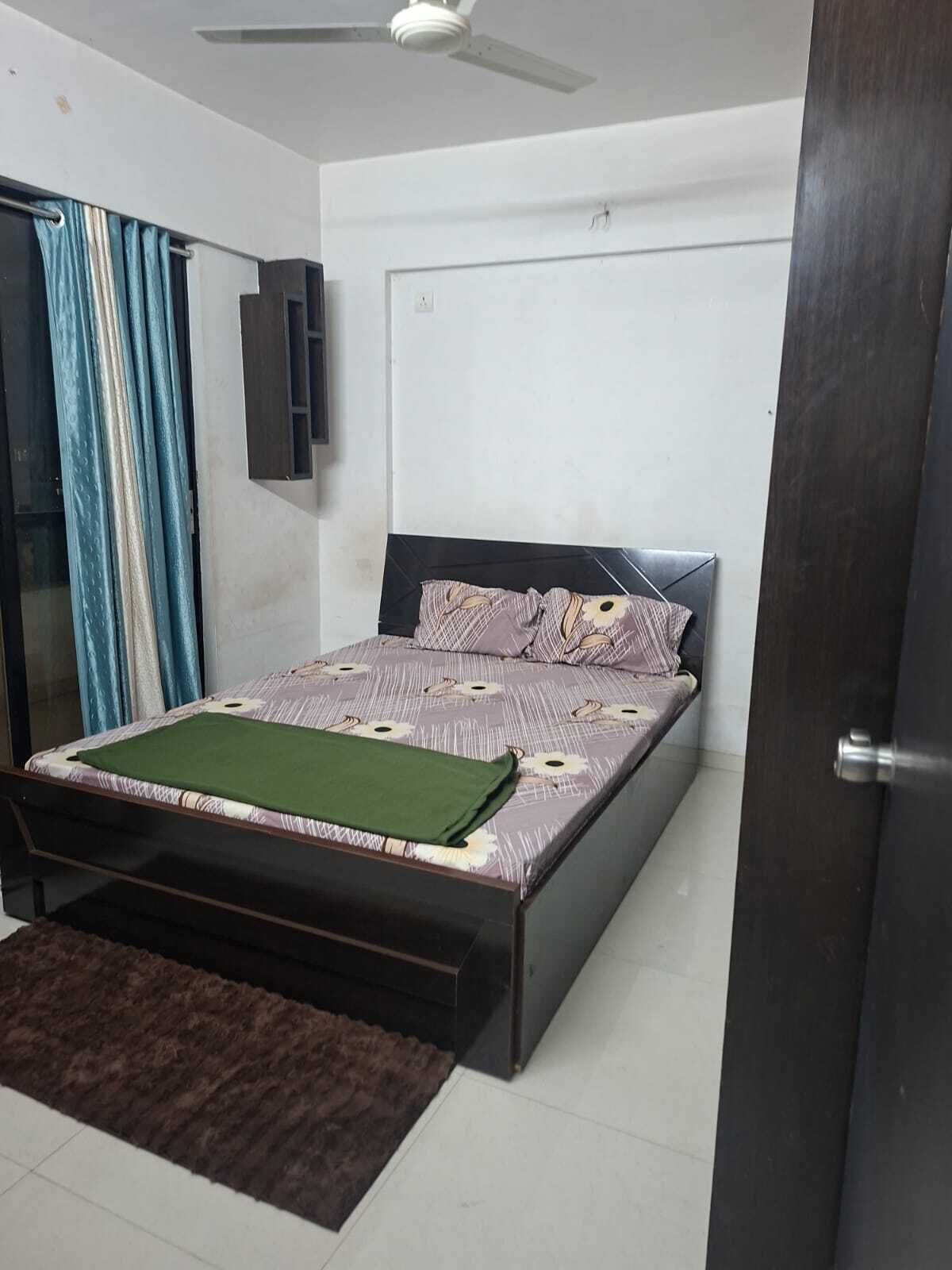 A bedroom with a bed, a ceiling fan, a door, and a window with curtains.
