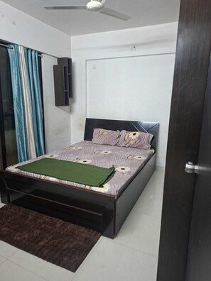Une chambre à coucher avec un lit, un ventilateur de plafond, une porte et une fenêtre avec des rideaux.