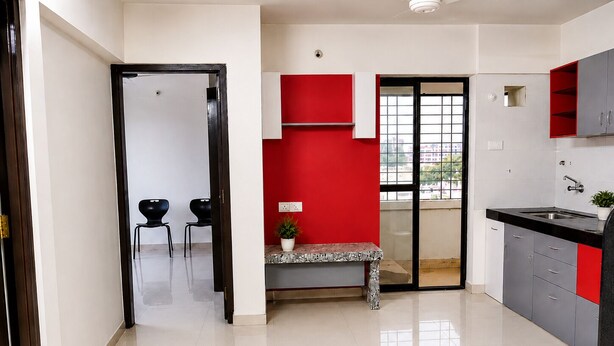 A modern kitchen with a red accent wall, a dining area with two chairs, and a view through a glass door.