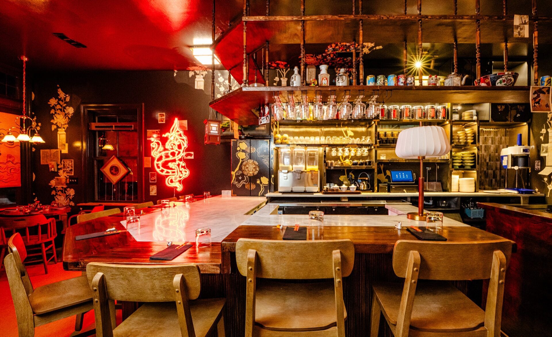 A bar area with wooden chairs, a bar counter, and shelves with bottles and glasses.