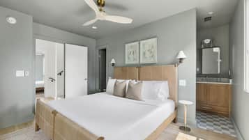A bedroom with a bed, bedside tables, a ceiling fan, a bathroom with a sink and mirror, and a checkered floor.