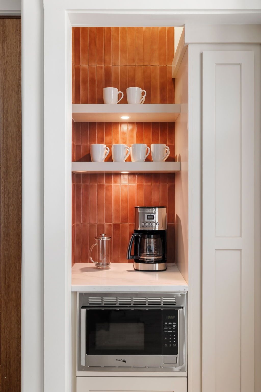 A kitchen with a coffee maker, microwave, and shelves with cups.