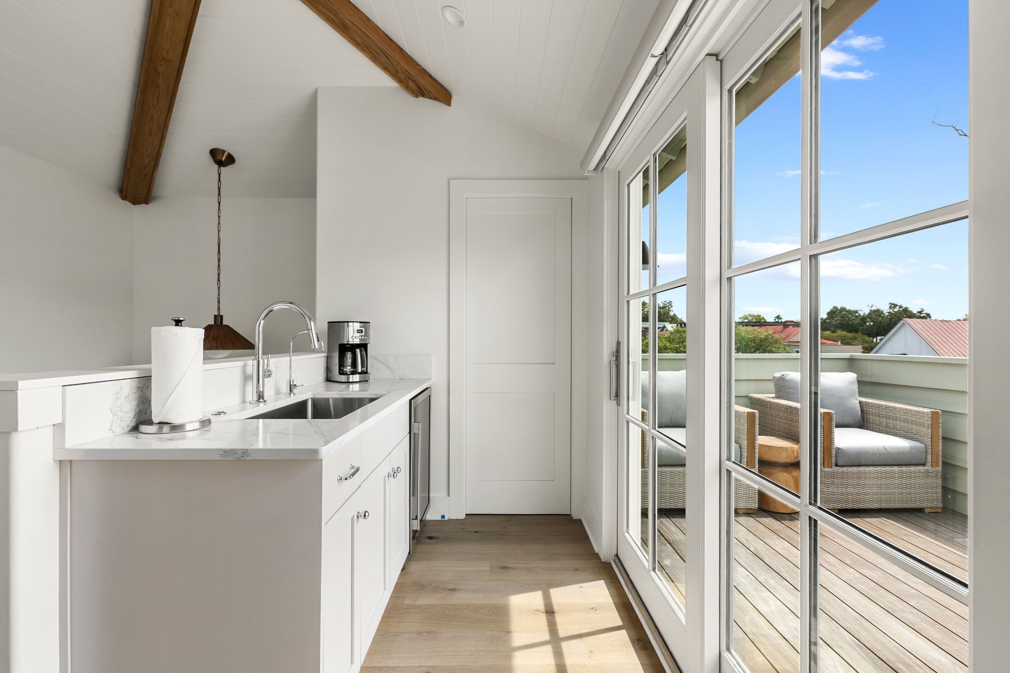 A narrow kitchen with a white countertop, a coffee maker, and a hanging light fixture.