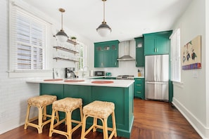 A kitchen with a central island, green cabinets, and a stainless steel refrigerator. - Smalls Alley (Charleston)