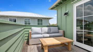A deck with a wooden table and a grey sofa, green walls, and a white building in the background.