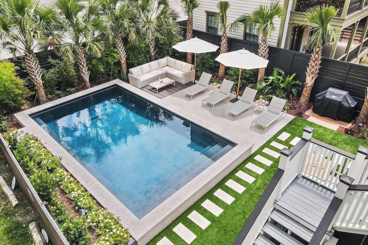 Ein rechteckiger Swimmingpool mit einer umlaufenden Sonnenterrasse, Liegestühlen und Sonnenschirmen.