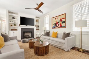 A modern living room with a fireplace, a television, a sofa set, and a ceiling fan. - Smalls Alley (Charleston)