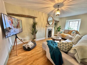 A living room with a fireplace, a television on a tripod, a sofa, and a large mirror. - Muddy Boots Arcade Royale (Kirkby Stephen)
