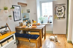 A cozy dining area with a wooden table set for a meal, a bench, and a dog resting nearby. - Muddy Boots Arcade Royale (Kirkby Stephen)