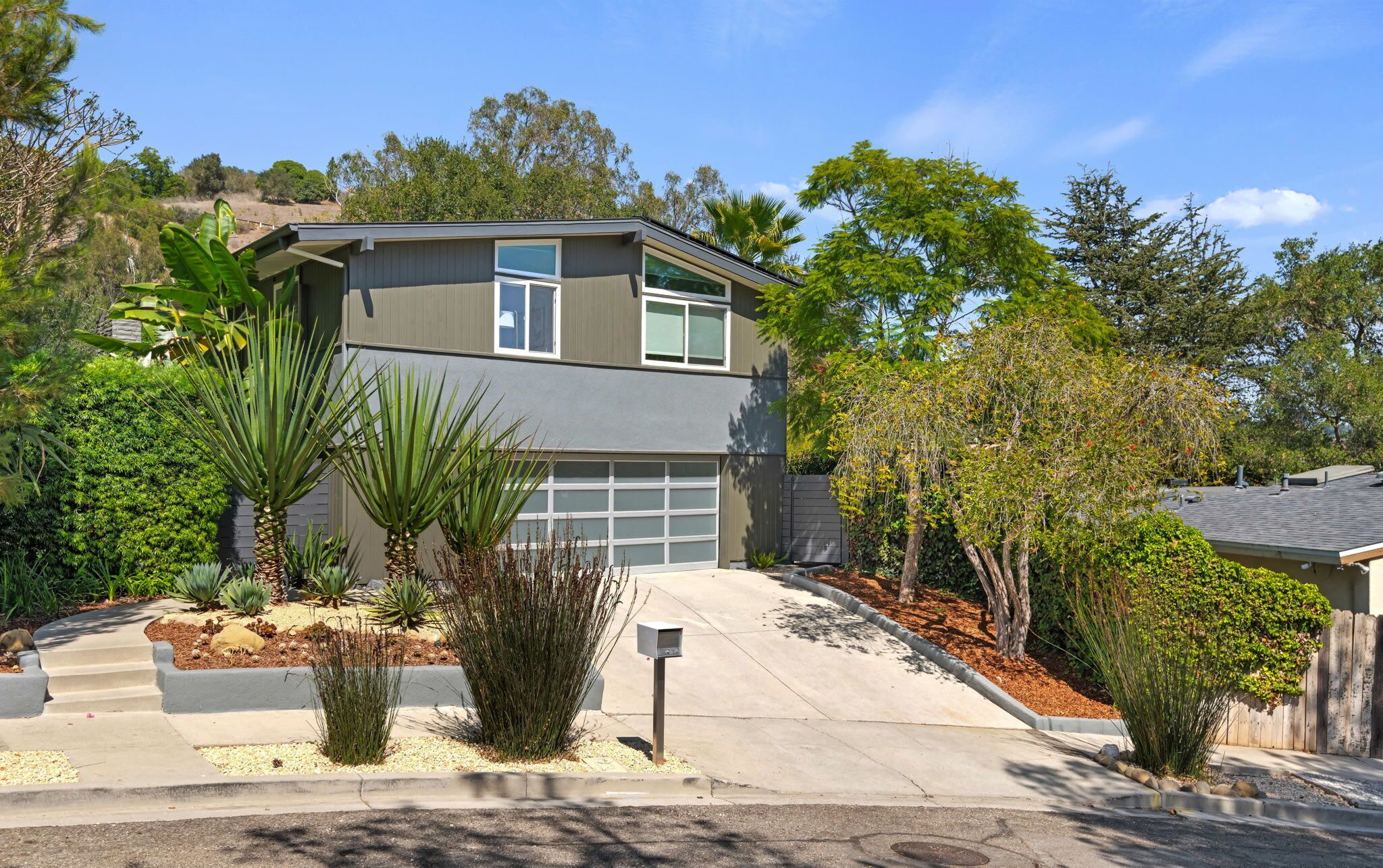 A two-story residential house with a garage, surrounded by landscaped gardens and trees.