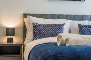 A neatly made bed with a grey headboard, white and blue patterned pillows, and a bedside lamp on a nightstand. - Luxury 2-Bedroom Apartment Near Slough Station | Sleeps 8 | Balcony (Slough)