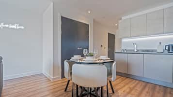 A modern kitchen with a dining area, featuring a table set for two with wine glasses and plates, and a kitchen counter with a coffee machine.