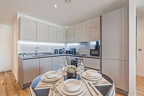 A modern kitchen with a central island, built-in appliances, and a dining area set for a meal. - Luxury 2-Bedroom Apartment Near Slough Station | Sleeps 8 | Balcony (Slough)
