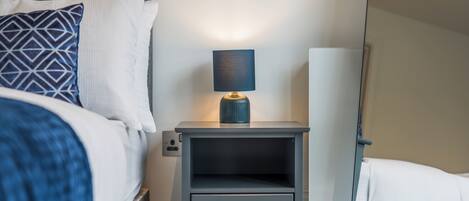 A neatly made bed with a patterned pillow, a bedside table with a lamp, and a drawer.