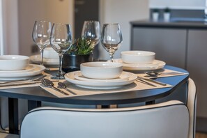 A dining table set with white plates, bowls, and cutlery, accompanied by wine glasses and a potted plant. - Luxury 2-Bedroom Apartment Near Slough Station | Sleeps 8 | Balcony (Slough)