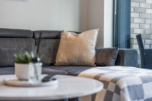 Un sofá modular con un cojín, una mesita con una planta y un plaid escocés.