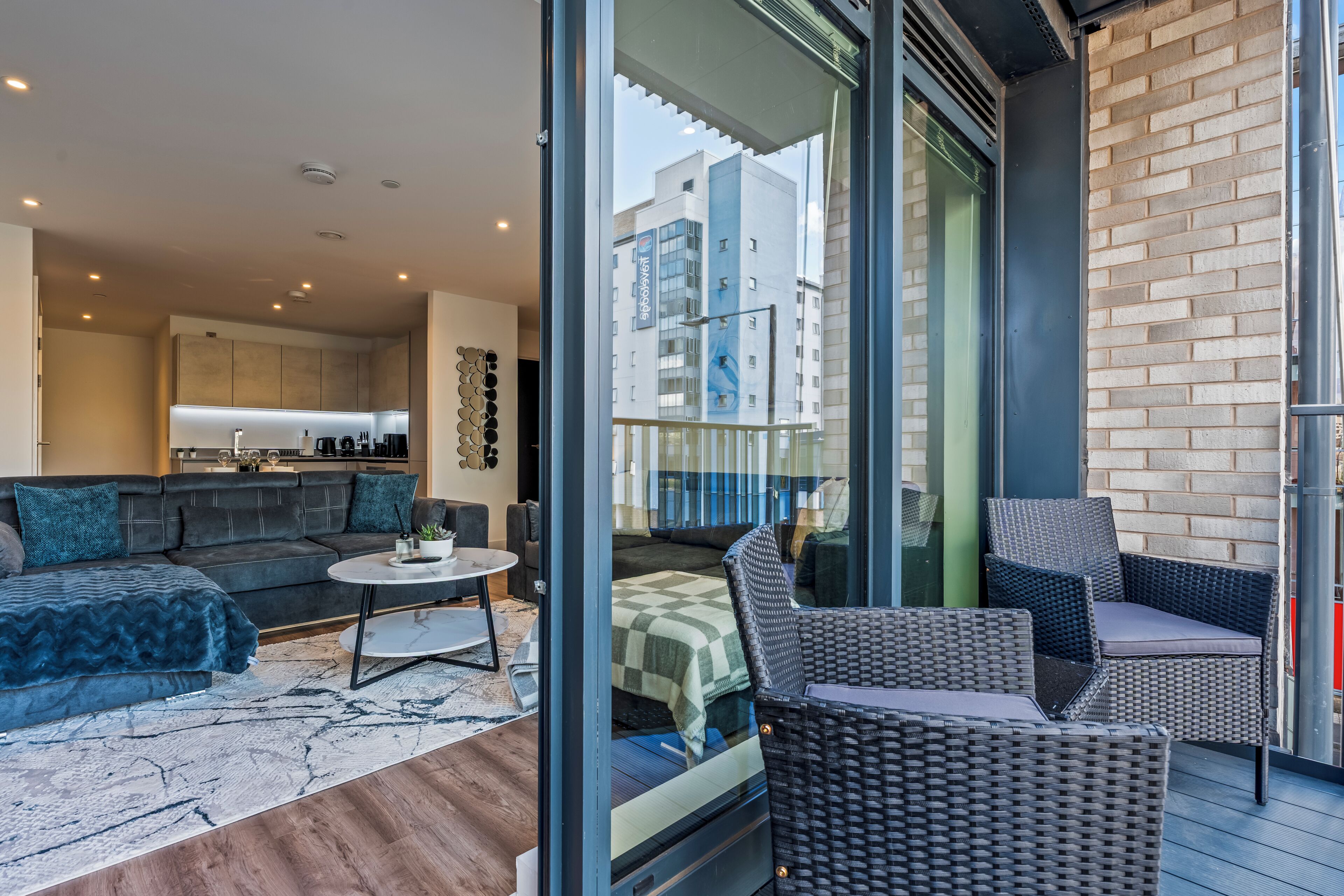 A modern living room with a sofa, a coffee table, and a balcony with wicker furniture.