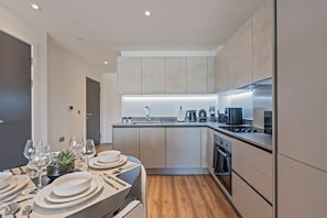 A modern kitchen with a central island, built-in appliances, and a dining area set for a meal. - Luxury 2-Bedroom Apartment Near Slough Station | Sleeps 8 | Balcony (Slough)