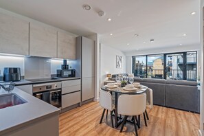 A modern kitchen with built-in appliances and a dining area with a table set for four. - Luxury 2-Bedroom Apartment Near Slough Station | Sleeps 8 | Balcony (Slough)