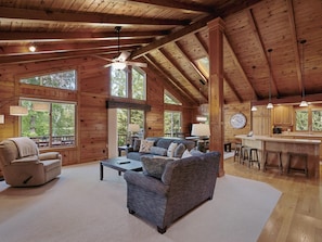 A spacious cabin interior with a high ceiling, wooden beams, a large sofa, a dining area, and a kitchen with bar stools. - NEW on Lake Ossie! Hot Tub | Sauna| Great Fishing (Pequot Lakes)