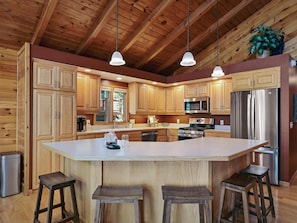 A kitchen with wooden cabinets, stainless steel appliances, a central island with stools, and pendant lighting. - NEW on Lake Ossie! Hot Tub | Sauna| Great Fishing (Pequot Lakes)
