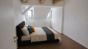 A bedroom with a bed, wooden beams, white walls, and a herringbone floor pattern. - Panoramic view! Charming 3-room apartment with a sauna and Wi-Fi (Chemnitz)