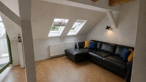 A spacious loft with a large black leather sofa, wooden beams, and skylights. - Panoramic view! Charming 3-room apartment with a sauna and Wi-Fi (Chemnitz)