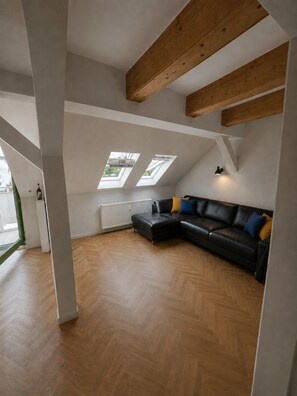 Um loft espaçoso com um amplo sofá de couro preto, vigas de madeira e claraboias.