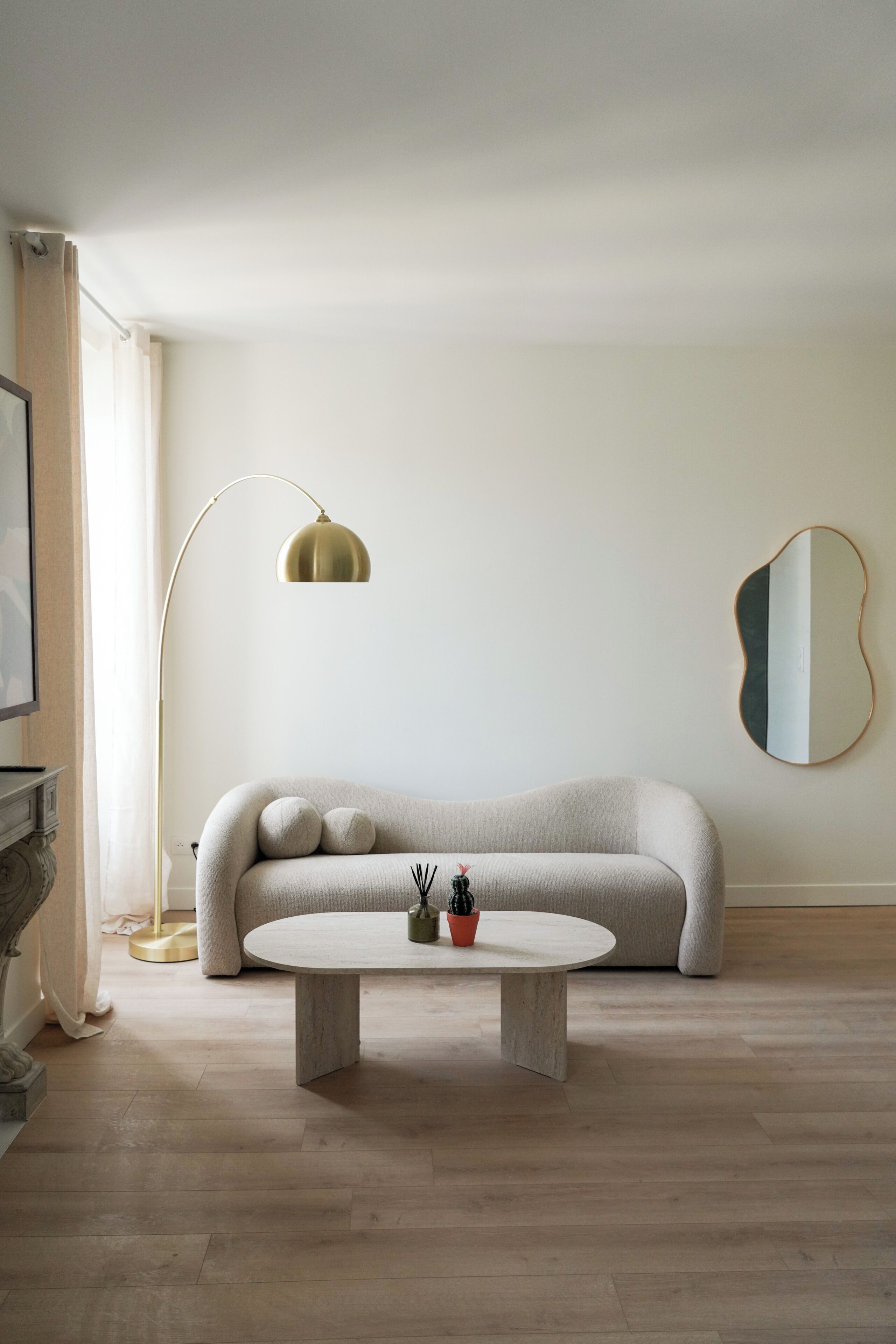 Een strak ingerichte woonkamer met een bank, een salontafel, een vloerlamp en een spiegel aan de muur.