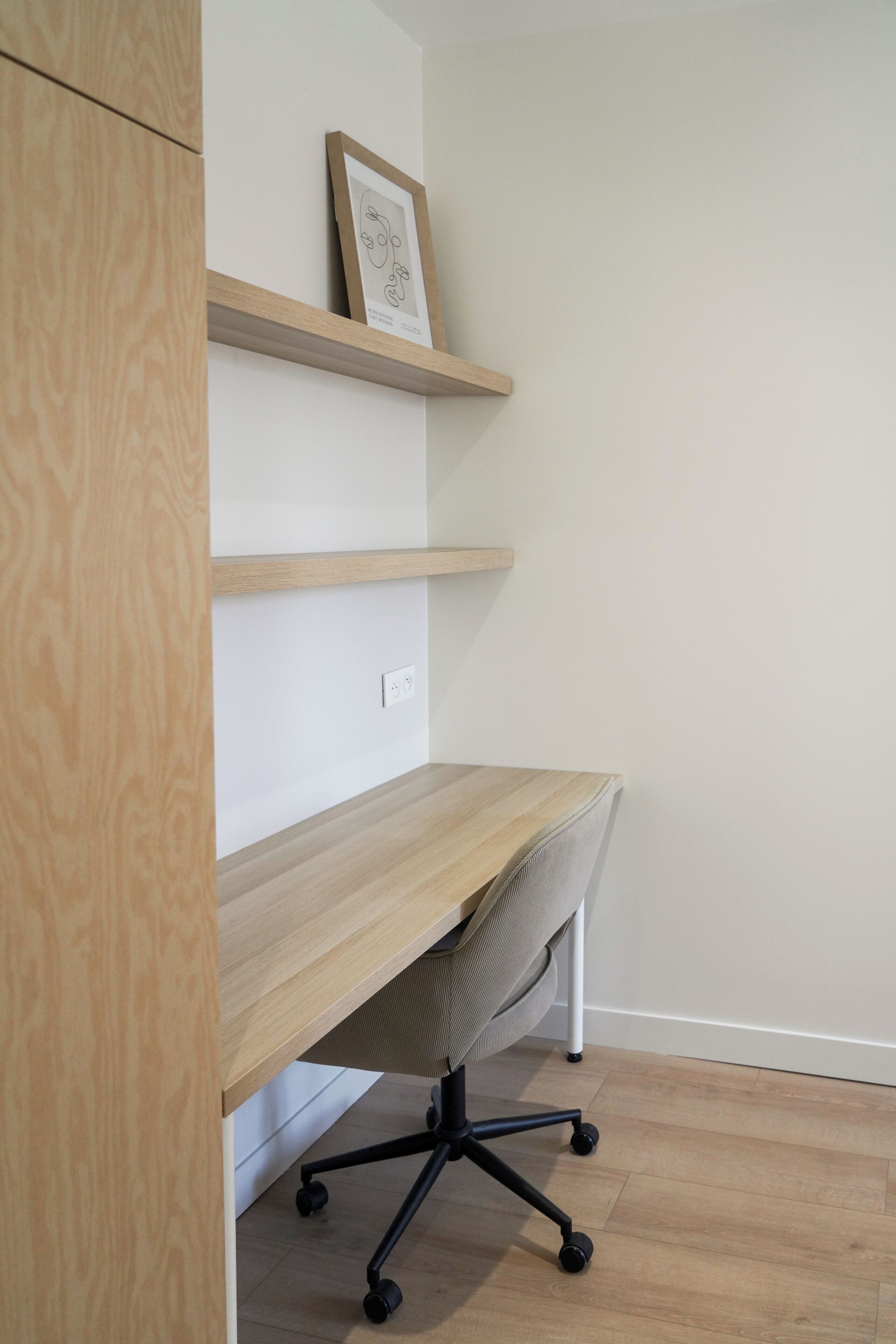 A workspace with a wooden desk, a chair, and a shelf with a framed picture.
