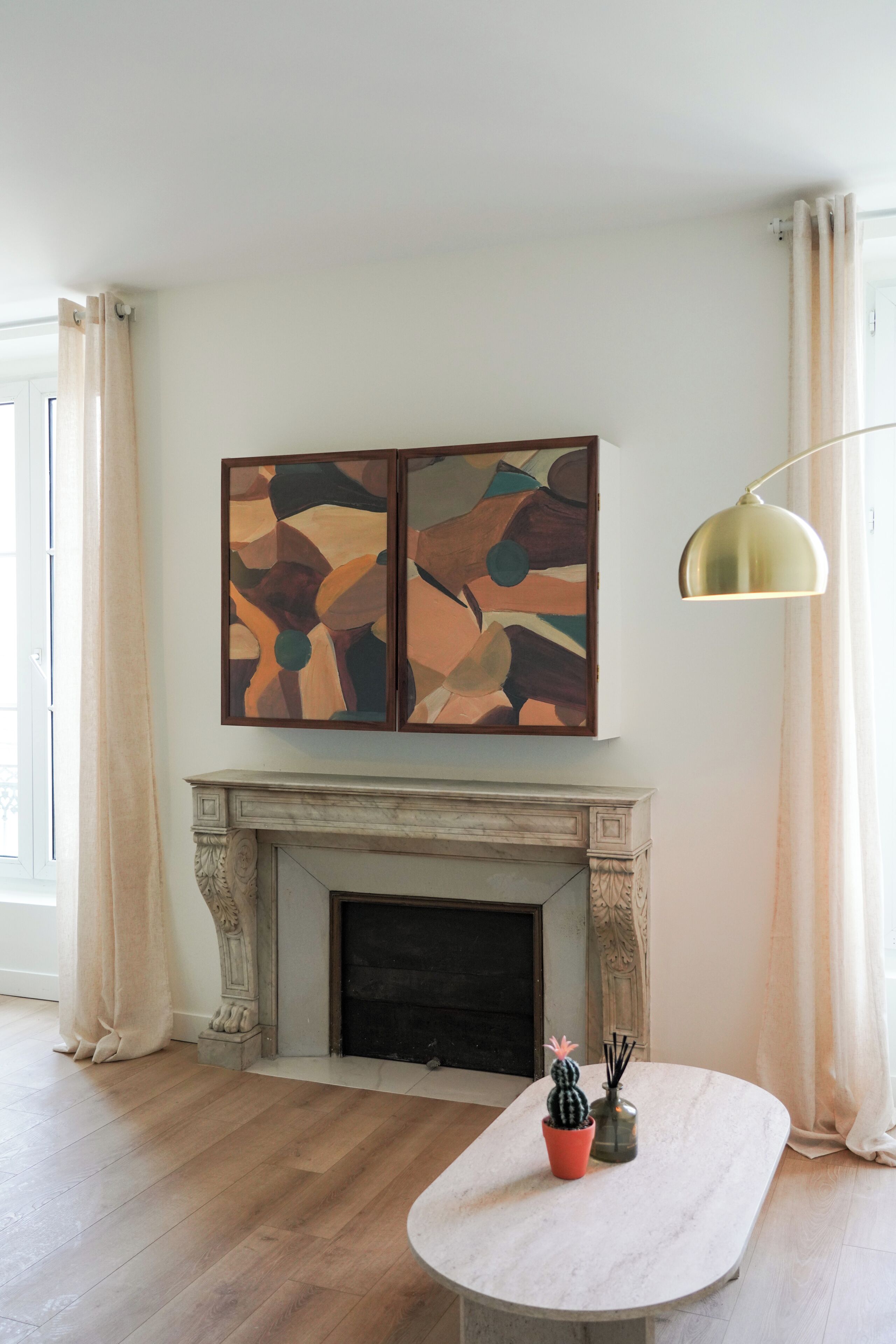 Una habitación con chimenea, una mesa de mármol con un cactus y un candelabro, y un cuadro abstracto moderno sobre la chimenea.
