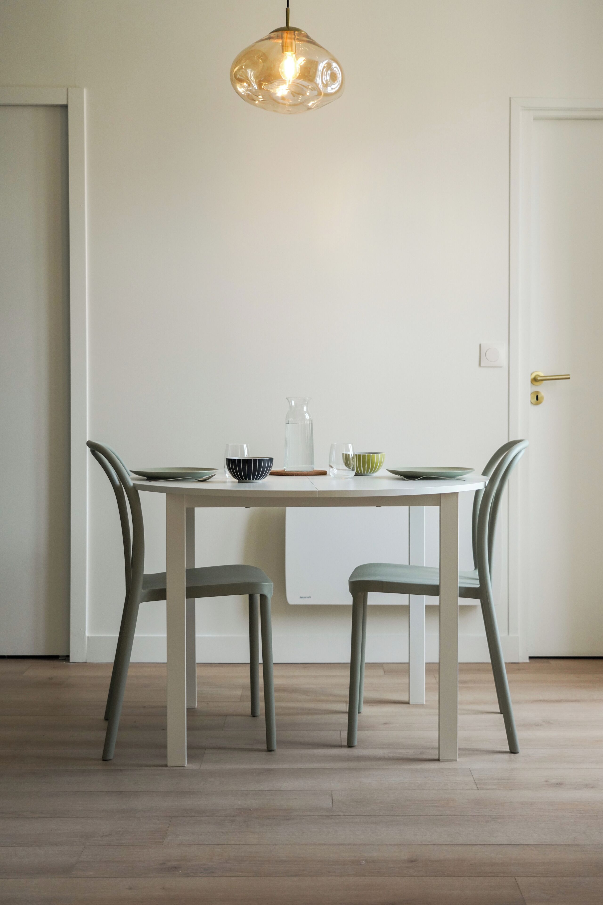 Una mesa de comedor con sillas, una lámpara colgante y una puerta al fondo.