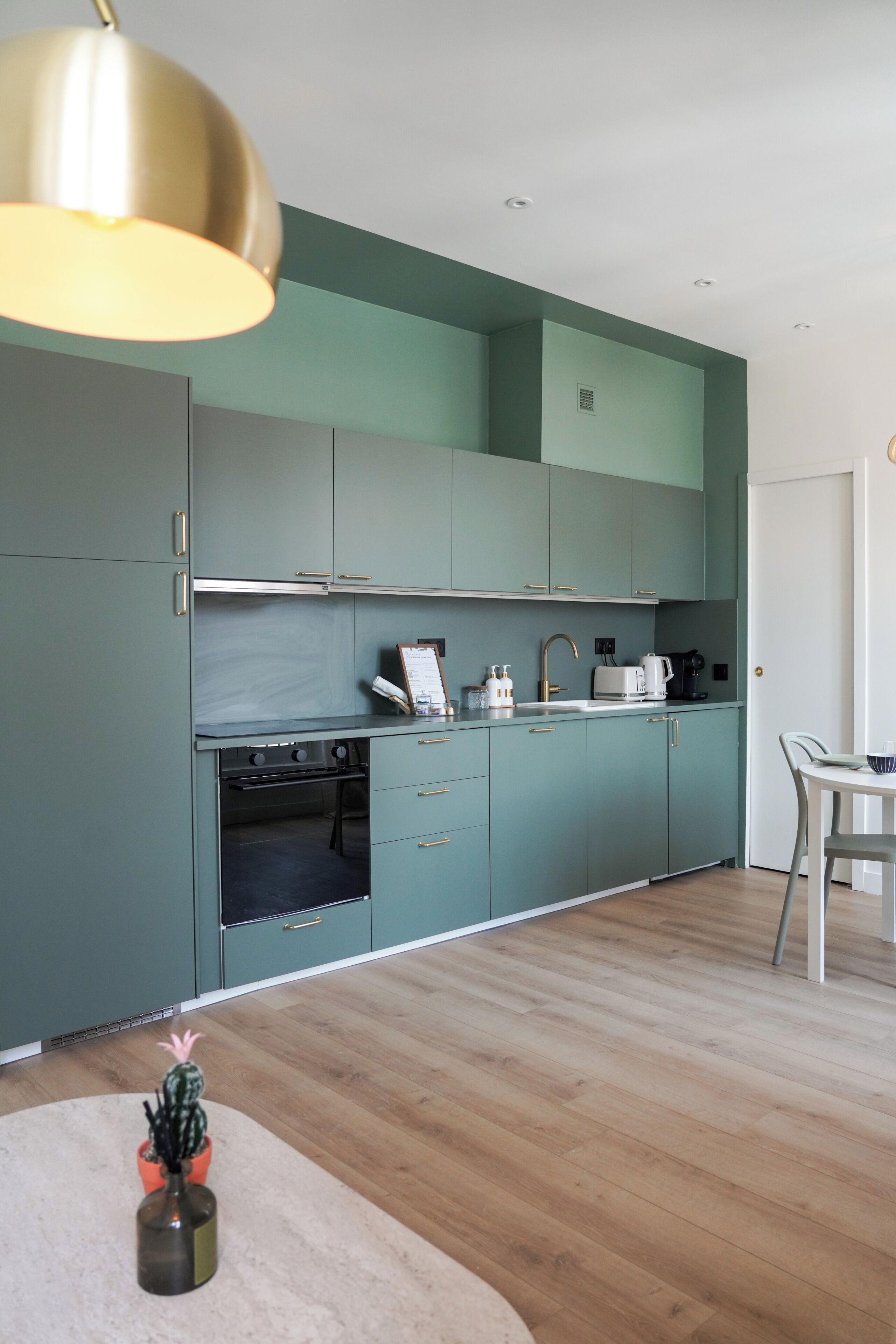 Een moderne keuken met blauwgroene kastjes, roestvrijstalen apparatuur en een houten vloer.