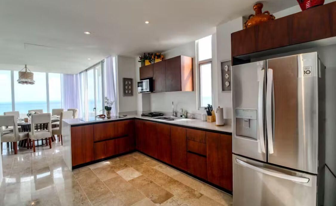 A modern kitchen with a large island, stainless steel appliances, and a view of the sea.
