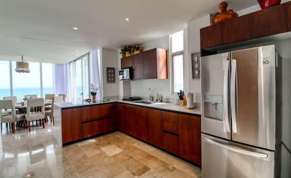 A modern kitchen with a large island, stainless steel appliances, and a view of the sea.