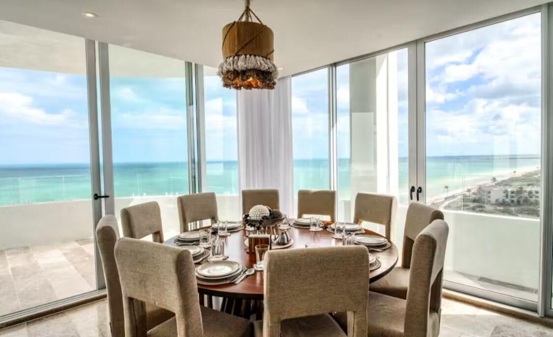 Une salle à manger offrant une vue panoramique sur l’océan, de grandes fenêtres et un lustre.