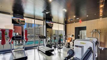 Ein modernes Fitnessstudio mit Cardiogeräten, Kurzhanteln und Blick auf eine Stadtkulisse durch große Fenster.