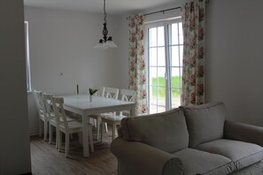 A dining area with a white table and chairs, a hanging light fixture, and a window with floral curtains.