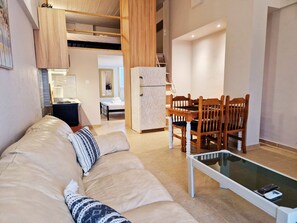 Ein modernes Wohnzimmer mit Sofa, Esstisch und Stühlen, einer Küchenzeile und einem separaten Schlafzimmer mit Bett.
