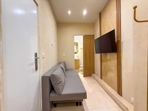 Um corredor com sofá, televisão na parede e uma porta.