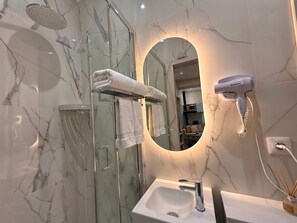 Ein modernes Badezimmer mit einer Duschkabine aus Glas, einem runden Spiegel, einem Fön und einem Waschbecken mit Marmorverkleidung.