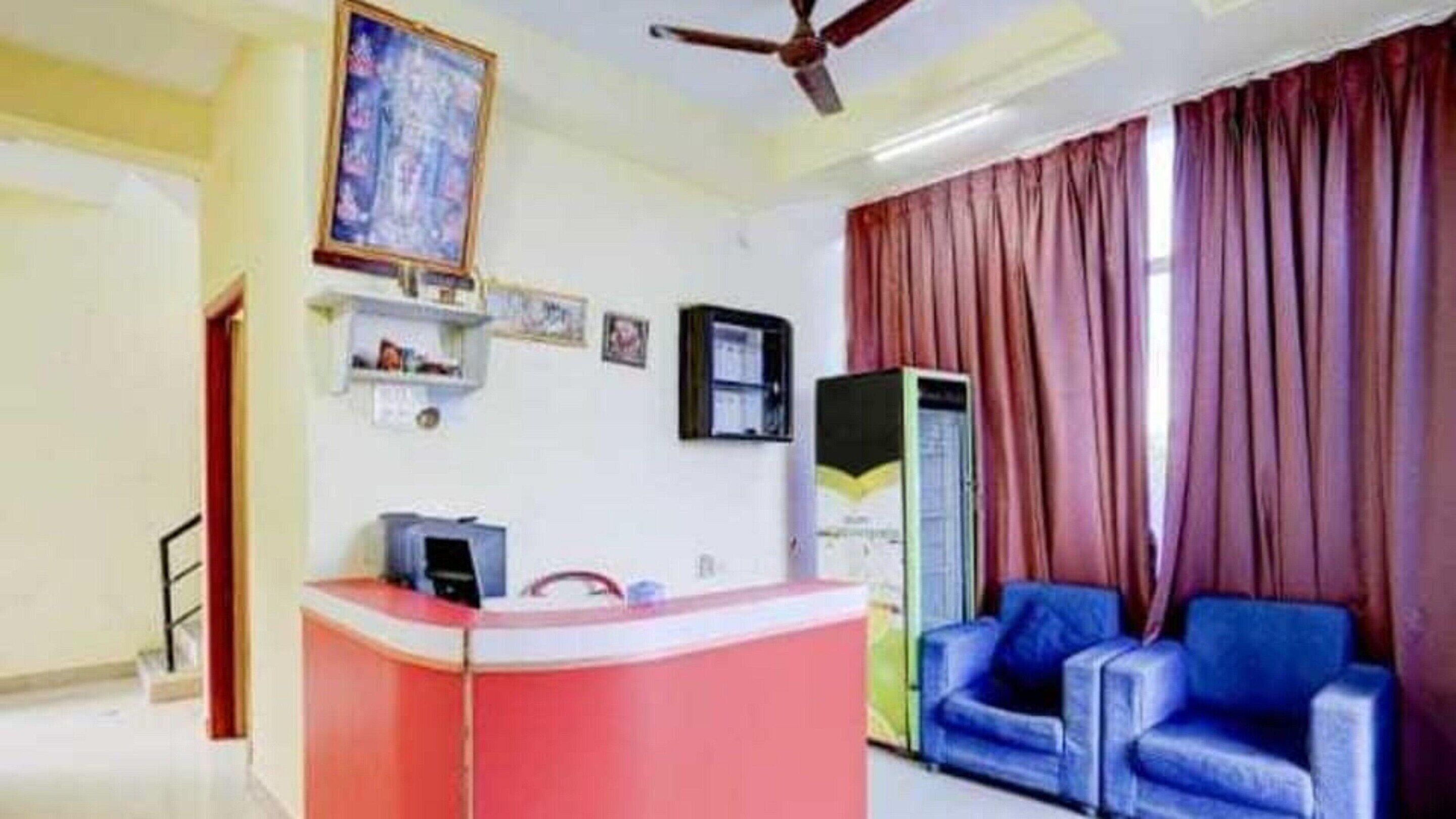 A room with a reception desk, a ceiling fan, a large window with curtains, and a blue sofa.